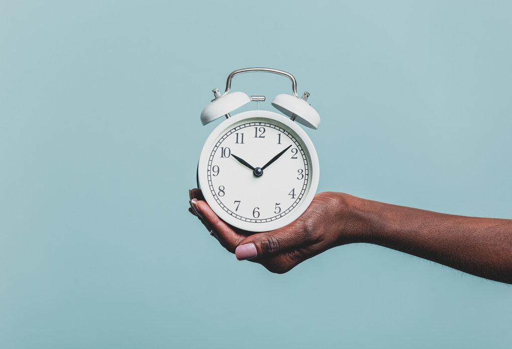 Black female hand hold alarm clock on blue background