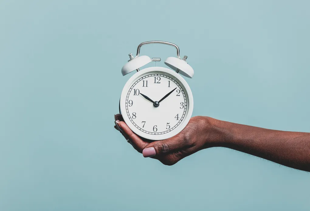 Black female hand hold alarm clock on blue background